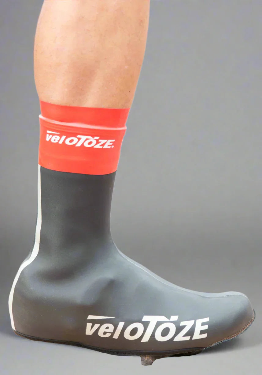 Red and black waterproof cycling shoe cover with veloToze logo on a person's leg