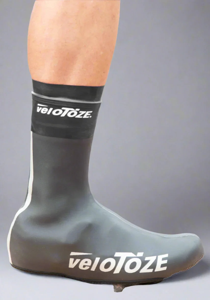 Black cycling shoe cover on foot, waterproof, with veloToze logo, gray background